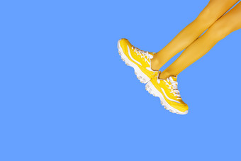 新黄色的女运动鞋长女人腿黄色的连裤袜孤立的蓝色的背景单色流行艺术概念横幅与复制空间新黄色的女运动鞋长女人腿黄色的连裤袜孤立的蓝色的背景