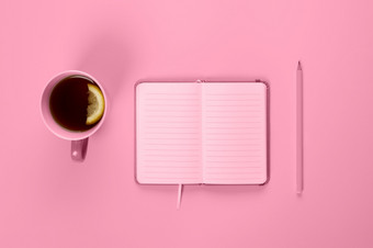 茶杯和花俏的笔记本与空空白页面桌子上从以上规划和设计概念前视图平躺复制空间模拟健美的粉红色的茶杯和花俏的笔记本与空空白页面桌子上从以上规划和设计概念