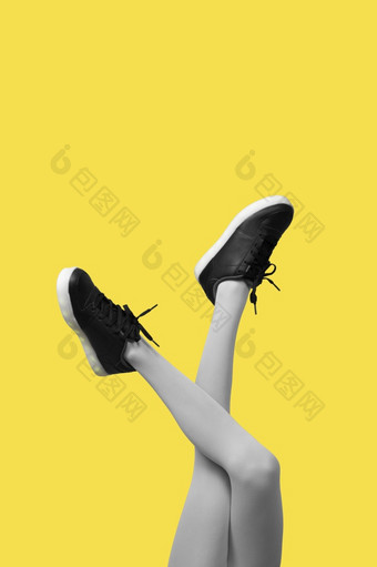 新黑色的女运动鞋长纤细的女人腿灰色的连裤袜孤立的黄色的背景有创意的流行艺术概念垂直横幅新黑色的女运动鞋长纤细的女人腿灰色的连裤袜孤立的黄色的背景
