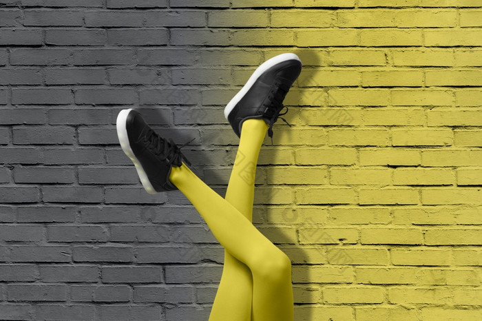 新黑色的女运动鞋长纤细的女孩腿黄色的连裤袜背景梯度黄色的和灰色的砖墙颜色一年流行艺术概念新黑色的女运动鞋长纤细的女孩腿黄色的连裤袜背景梯度黄色的和灰色的砖墙颜色一年概念