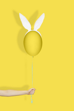 有创意的复活节最小的概念手持有黄色的蛋兔子耳朵就像气球字符串单色复活节有创意的复活节最小的概念手持有黄色的蛋兔子耳朵就像气球字符串单色复活节