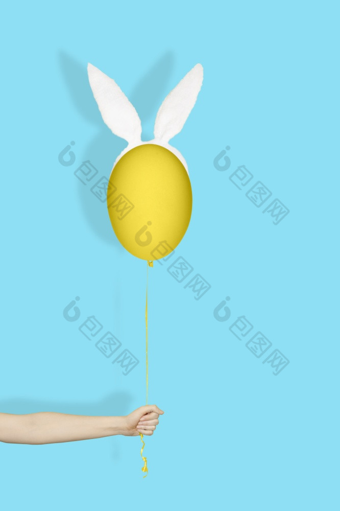 有创意的复活节最小的概念手持有黄色的蛋兔子耳朵就像气球字符串光蓝色的背景有创意的复活节最小的概念手持有黄色的蛋兔子耳朵就像气球字符串光蓝色的背景