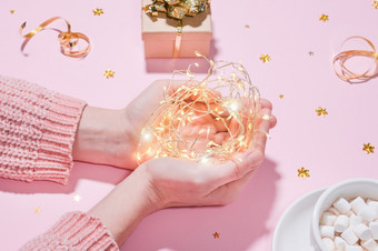 美丽的和舒适的假期概念手持有字符串加兰灯的背景包装礼物杯热巧克力可可与棉花糖金俗丽的孤立的粉红色的背景美丽的和舒适的假期概念手持有字符串加兰灯的背景包装礼物杯热巧克力可可与棉花糖金俗丽的孤立的粉红色的