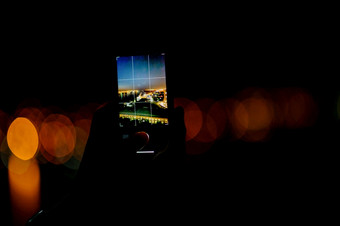 男人。需要照片的晚上城市智能手机拍摄的城市灯与移动设备晚上视图通过的屏幕的时间男人。需要照片城市晚上城市景观男人。需要照片的晚上城市智能手机
