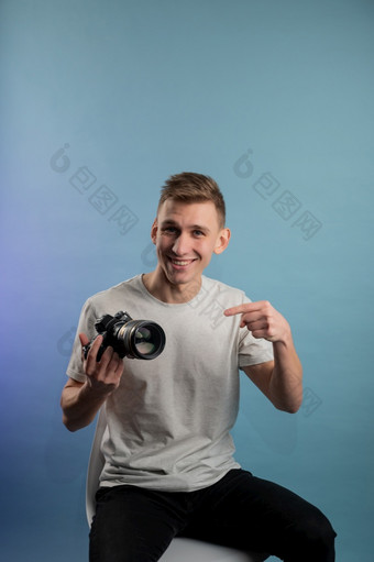 英俊的年轻的摄影师使用相机蓝色的背景男人。使用专业相机肖像的家伙看照片相机英俊的年轻的摄影师使用相机蓝色的背景