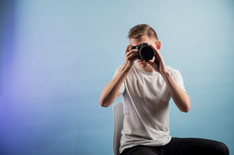 英俊的年轻的摄影师使用相机蓝色的背景男人。使用专业相机肖像的家伙看照片相机英俊的年轻的摄影师使用相机蓝色的背景