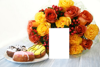 大美丽的花束黄色的和红橙色玫瑰和浆果灰色的木背景和下一个白色瓷板与三个多色的甜甜圈明信片布<strong>局</strong>的背景的花束