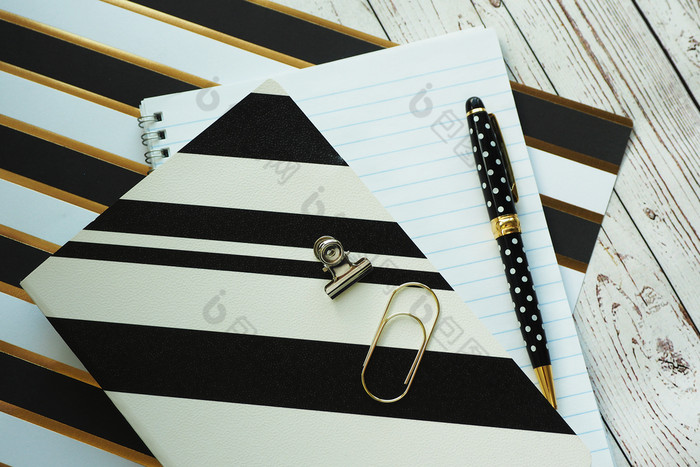 黑色的笔与波尔卡点笔记本和笔记本纸与黑色的和黄金条纹纸剪辑平原木背景