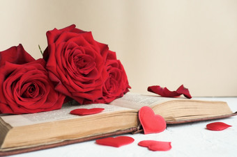 三个红色的玫瑰开放老书表格米色背景和很多红色的心