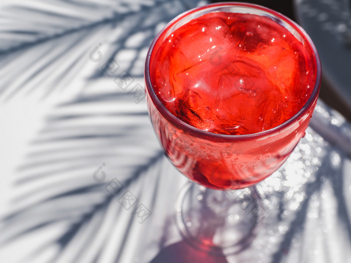 美丽的葡萄酒杯与粉红色的鸡尾酒和冰多维数据集站白色董事会对的影子棕榈叶子前视图特写镜头概念休闲和旅行美丽的玻璃与粉红色的鸡尾酒和冰
