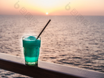 美丽的玻璃明亮的鸡尾酒与冰和稻草站的开放甲板对的背景海波和日落一边视图特写镜头概念休闲和旅行美丽的玻璃和明亮的鸡尾酒与冰