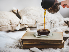 女手倒香咖啡杯的老书枕头和格子早餐的早期