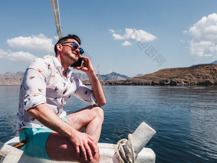 有吸引力的时尚男人。坐着船和拍摄沿海悬崖蓝色的天空和波概念休闲和旅行有吸引力的时尚男人。坐着船