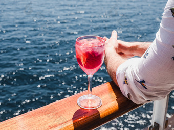 <strong>时尚男</strong>人。持有美丽的玻璃粉红色的酒的开放甲板巡航衬管对的背景蓝色的海波一边视图特写镜头概念休闲和旅行男人。持有美丽的玻璃粉红色的酒