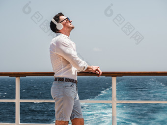 时尚男人。听音乐白色耳机的空甲板巡航衬管对的背景的海波一边视图特写镜头概念技术娱乐和旅行时尚男人。听音乐白色耳机