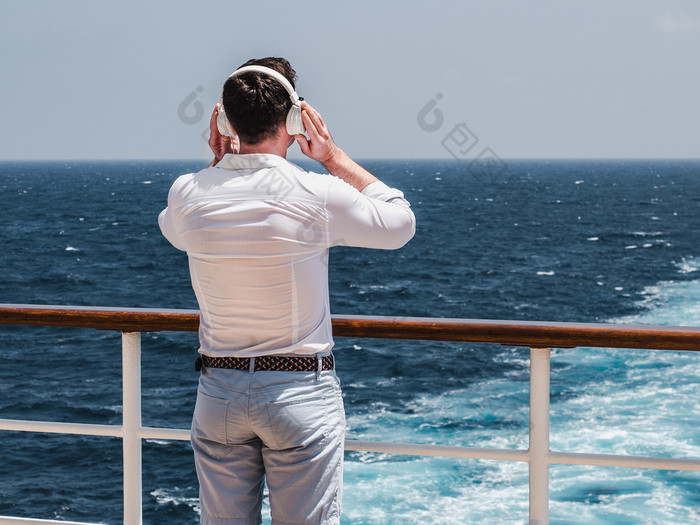 时尚男人。听音乐白色耳机的空甲板巡航衬管对的背景的海波一边视图特写镜头概念技术娱乐和旅行时尚男人。听音乐白色耳机