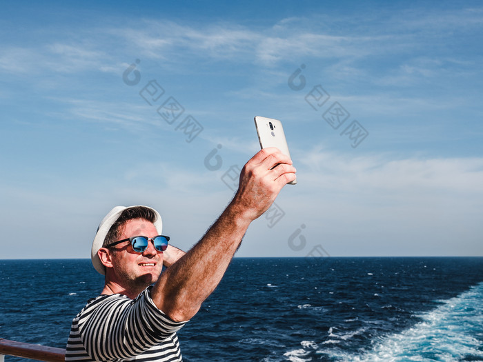时尚男人。持有移动电话的空甲板巡航衬管对的背景的海波一边视图特写镜头概念技术娱乐和旅行时尚男人。持有移动电话的甲板