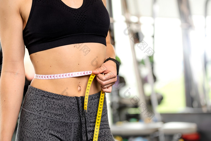 健康的生活方式概念女人后锻炼的健身房措施她的完美的腰围与测量磁带特写镜头