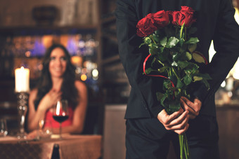 浪漫的惊喜概念男人。持有花束玫瑰和希望给女人在晚餐餐厅