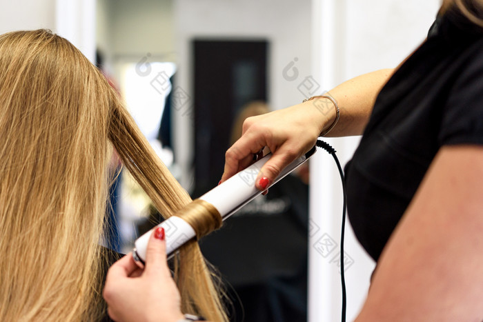 专业服务的美沙龙年轻的女人与美丽的金发碧眼的头发有使发型与卷曲铁