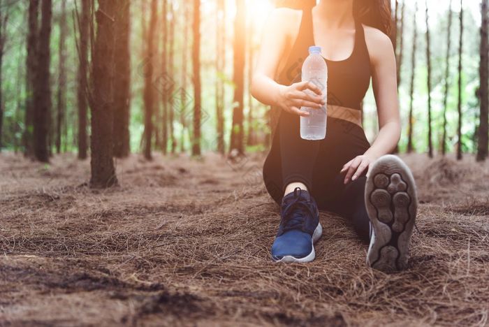 关闭美体育运动女人休息和持有喝水瓶和放松中间森林后累了从慢跑女孩坐着和看吸引力视图锻炼生活方式概念