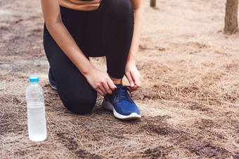 女人系鞋带当慢跑森林回来与喝水瓶旁边她的运动鞋绳子系人和生活方式概念医疗保健和健康主题公园和在户外主题