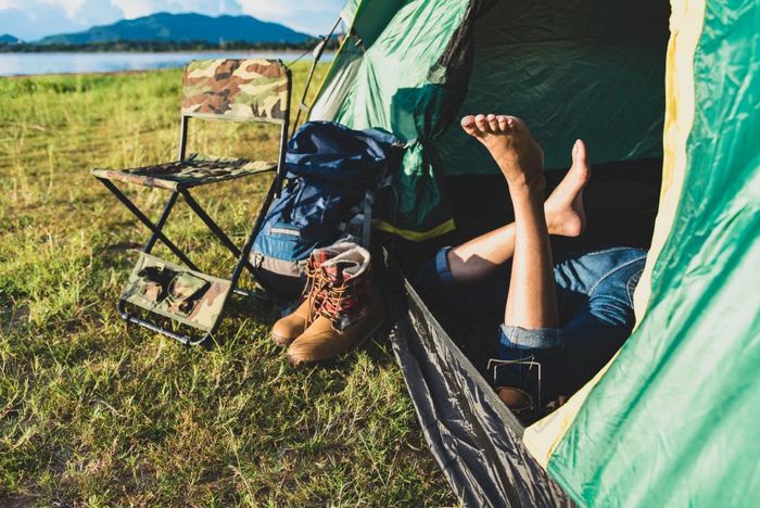 关闭女人腿放松野营帐篷与山湖和草地和草场背景生活方式和人概念野营和皮克内克主题绿色自然和夏天旅行主题