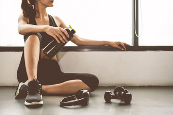 女人与哑铃和设备锻炼生活方式锻炼健身房健身打破放松后体育运动培训与蛋白质摇瓶背景健康的生活方式健身和运动员肌肉