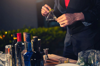专业酒保准备新鲜的石灰柠檬水鸡尾酒喝酒玻璃与冰晚上酒吧泡吧计数器占领和人生活方式概念户外背景