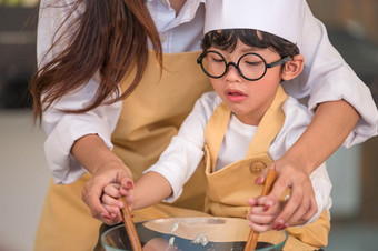 快乐可爱的小男孩与眼镜和美丽的亚洲妈妈。准备烹饪厨房首页人生活方式和家庭自制的食物和成分概念两个泰国人生活