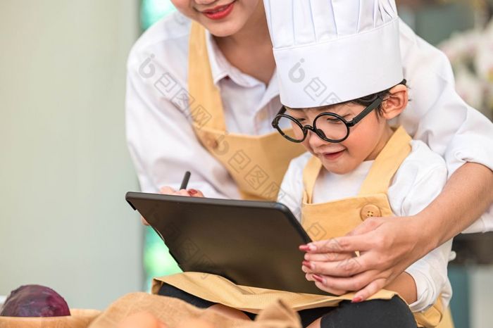 美丽的亚洲女人和可爱的小男孩准备在线购物和清单成分为烹饪厨房首页与平板电脑人生活方式和家庭自制的食物和成分概念