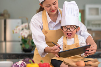 美丽的亚洲女人和可爱的小男孩准备在线购物和清单成分为烹饪厨房首页与平板电脑人生活方式和家庭自制的食物和成分概念