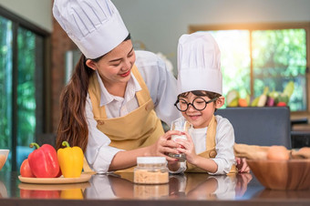 亚洲妈妈。帮助可爱的小男孩喝牛奶玻璃首页厨房老板烹饪统一的人生活方式和快乐家庭在一起概念钙和蛋白质牛奶营养