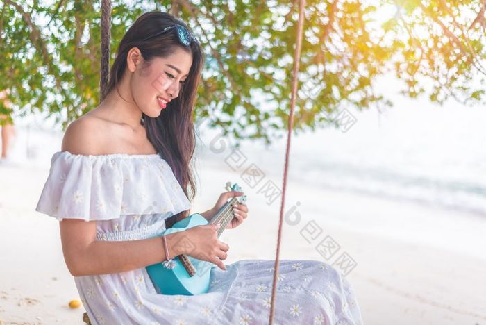 美丽的年轻的亚洲女人玩与尤克里里琴和放松的海滩人和假期概念假期和幸福生活概念夏天和海滩主题