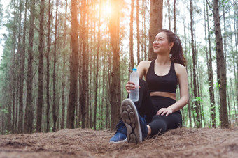 美亚洲体育运动<strong>女人休息</strong>和持有喝水瓶和放松中间森林后累了从慢跑女孩坐着和看吸引力视图锻炼概念生活方式主题