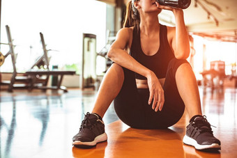 体育运动女人放松休息后锻炼锻炼健身健身房坐着和<strong>喝</strong>蛋白质摇<strong>喝水</strong>地板上强度培训和健美运动员肌肉主题温暖的和很酷的语气