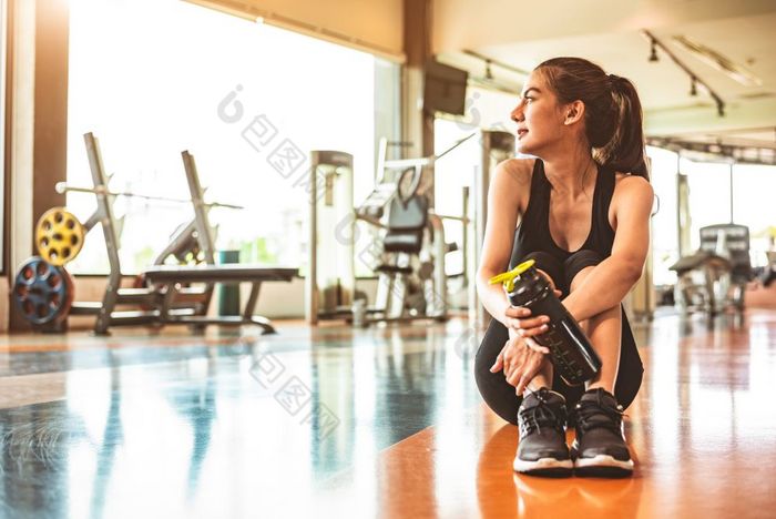 体育运动女人放松休息后锻炼锻炼健身健身房坐着和喝蛋白质摇喝水地板上强度培训和健美运动员肌肉主题温暖的和很酷的语气