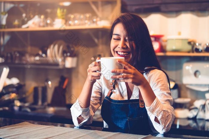 快乐亚洲女咖啡师持有杯咖啡和品尝酿造咖啡从自己与咖啡馆餐厅背景女服务员自助餐厅食物和喝人生活方式和占领概念