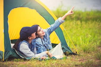 两个关闭朋友亚洲友谊放松野营帐篷绿色草地湖一边视图背景女孩指出手指天空人生活方式旅行假期概念夏天野餐活动
