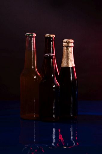 四个啤酒瓶黑色的和紫色的背景与反射闪亮的蓝色的表面四个啤酒瓶黑色的和紫色的背景与反射闪亮的蓝色的表面