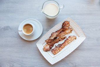 炸培根白色板与杯咖啡和牛奶壶早餐灰色的表格炸培根白色板与杯咖啡和牛奶壶