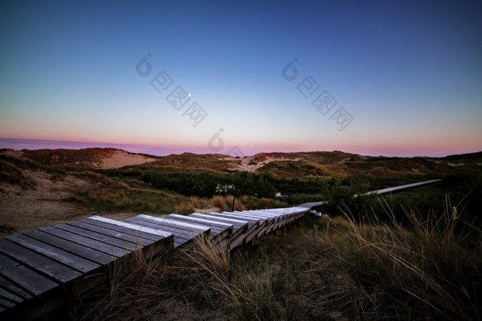 步骤沿海木木板路后日落与色彩斑斓的紫色的天空在滚动沙子沙丘和沿海植被夏天假期假期海概念