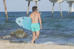 年轻的有吸引力的冲浪者持有他的冲浪板的海滩