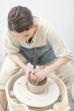 年轻的女坐着表格和使粘土陶瓷杯子她的工作工作室