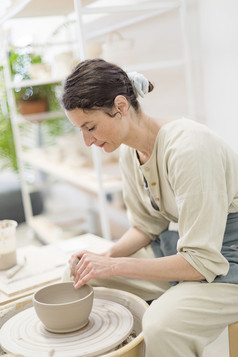 年轻的女坐着表格和使粘土陶瓷杯子她的工作工作室
