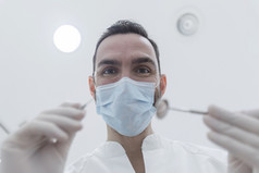 牙医穿外科手术面具而持有的角度镜子和钻准备好了开始