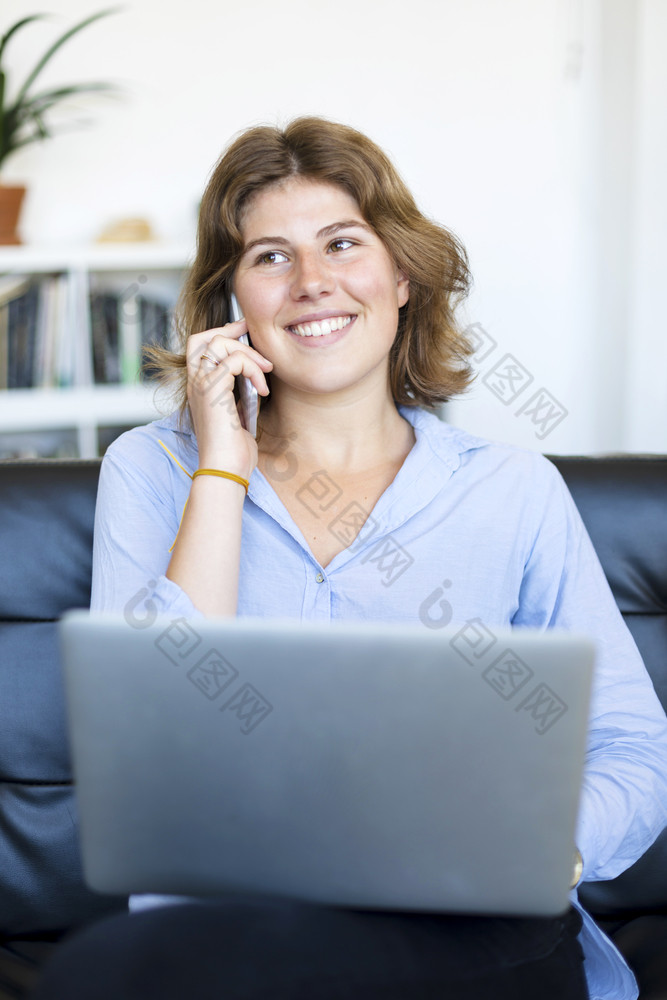 企业家女人穿蓝色的衬衫工作与移动PC坐着沙发上首页