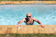 肖像英俊的男人。休息的边缘游泳池穿太阳镜夏天假期概念