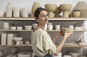 陶艺家女人持有波特她的工作室年轻的女陶艺家在室内持有手工制作的粘土产品概念陶器