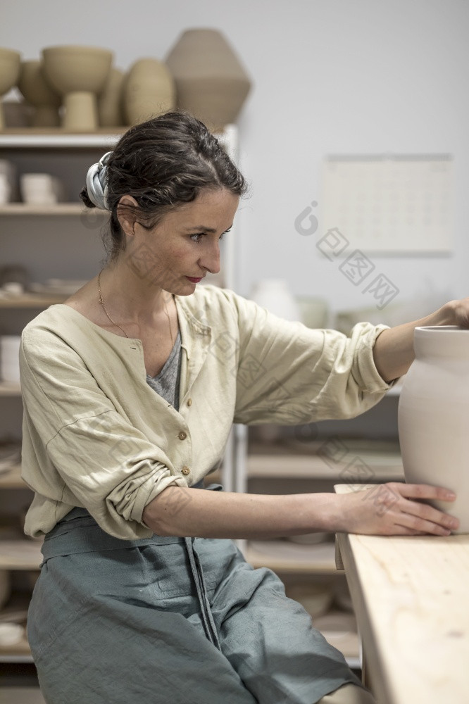 女人持有陶器仪器为刮平滑塑造和雕刻夫人选址板凳上与陶器轮和使粘土能
